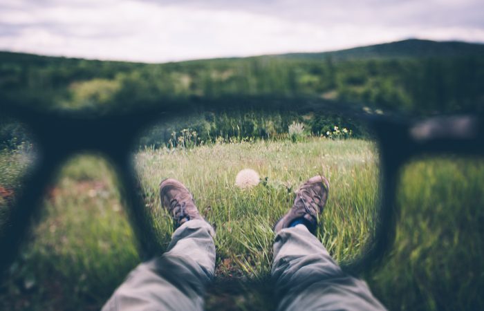 view of feild through glasses with feet and flower through lens