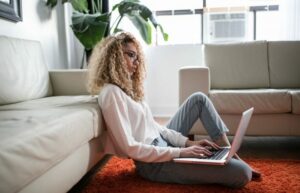 Woman sitting on carpet in living room working on laptop