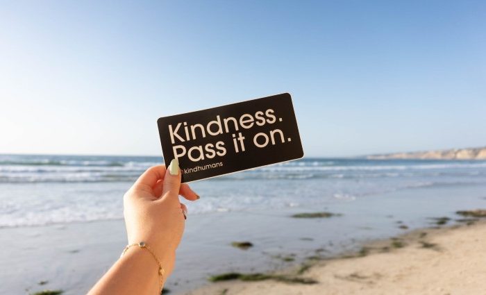 A girl holding a sign saying 'Kindness pass it on'
