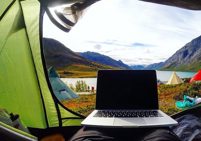 A person sitting in a tent with a laptop and a view of the mountains