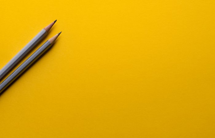 two gray pencils laying on yellow surface