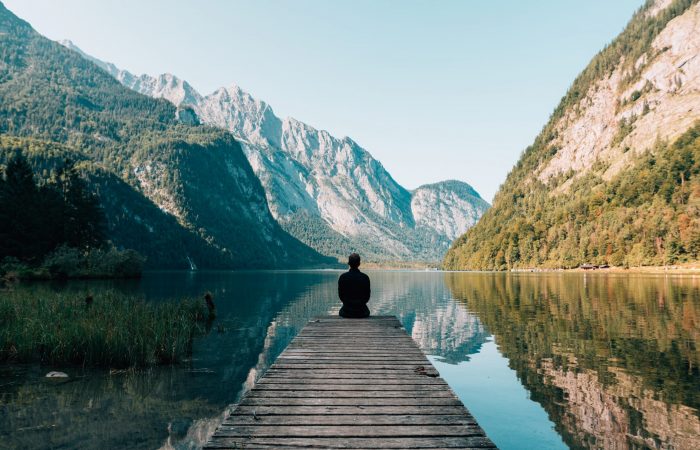 a person sitting at the end of a dock at a lake with mountains
