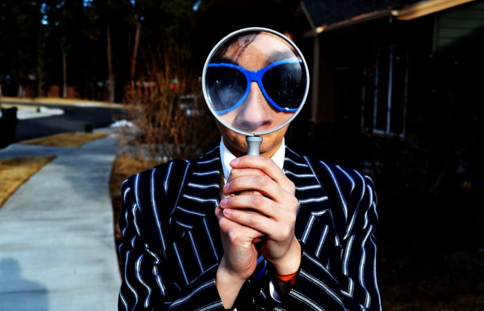 Woman with dark blue glasses looking through a magnifying glass