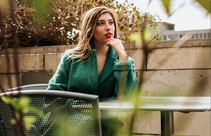 Woman in green trench coat sitting at a table thinking
